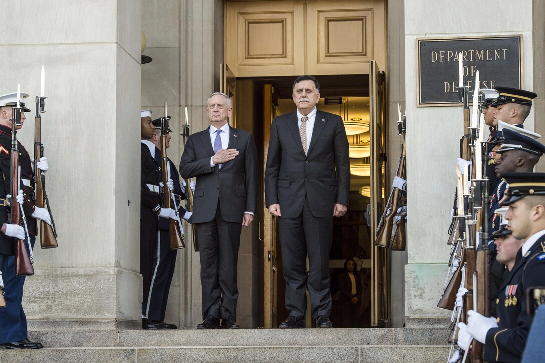 Defense Secretary Jim Mattis and the Libyan prime minister stand at a Pentagon entrance, flanked by honor guard members.