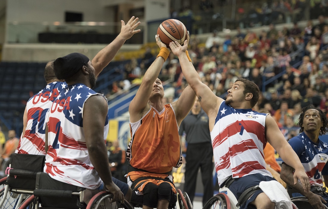 Four athletes in wheelchairs reach up for a basketball.