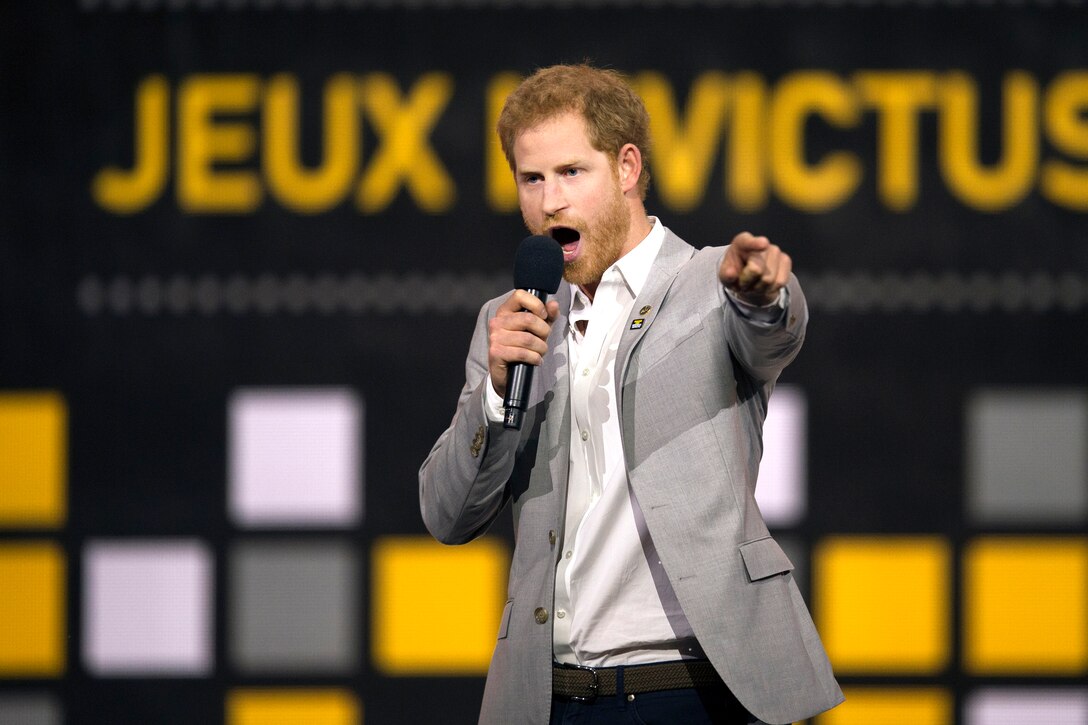 Britain’s Prince Harry stands on a stage with Invictus Games logos behind him.