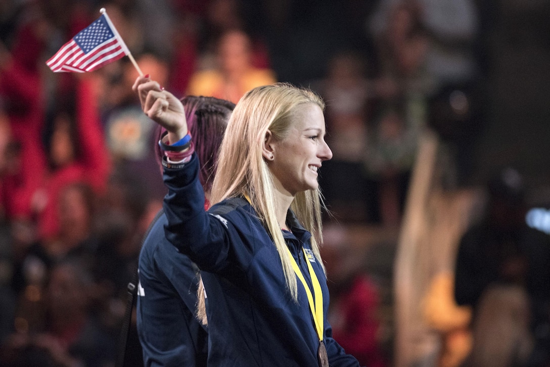 A member of Team U.S. waves an American flag as she walks across a stage.