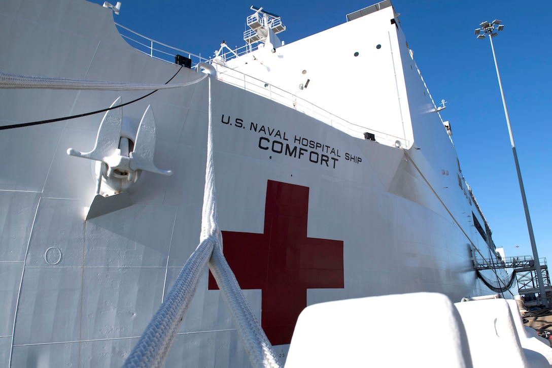 A red cross shows from a hospital ship at a pier.