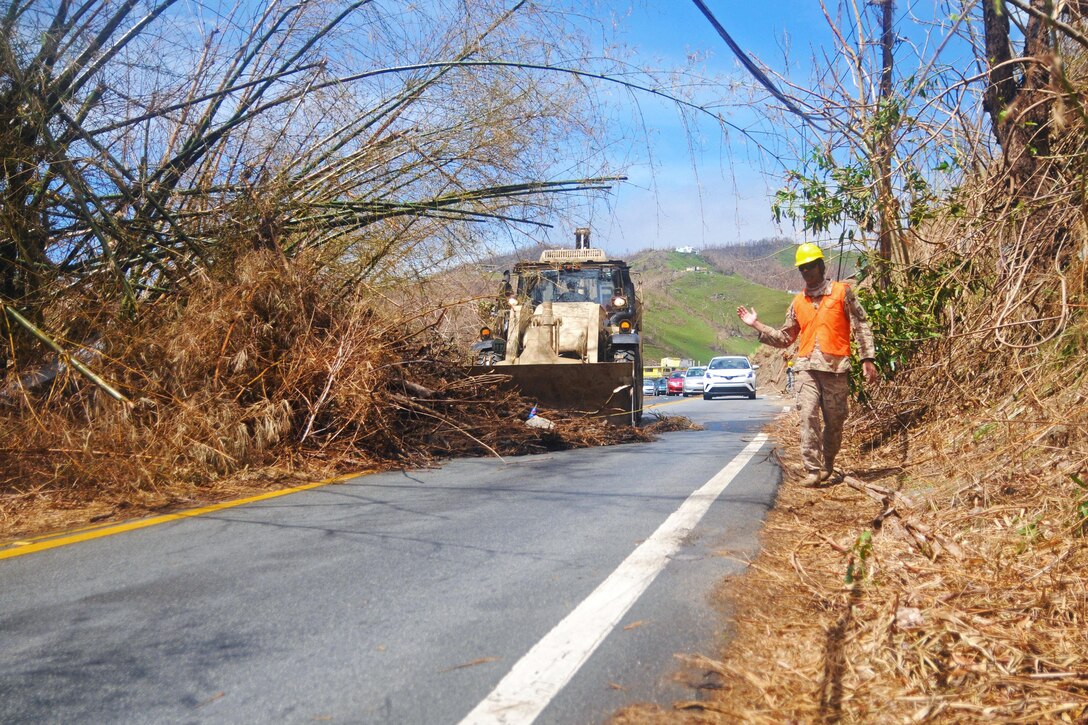 A Guardsman guides a bulldozer to clear debris and trees from roads.