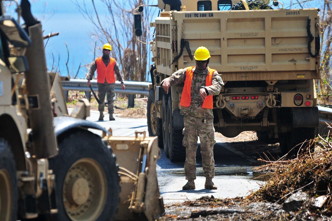 A Guardsman guides a bulldozer to remove debris from a road.