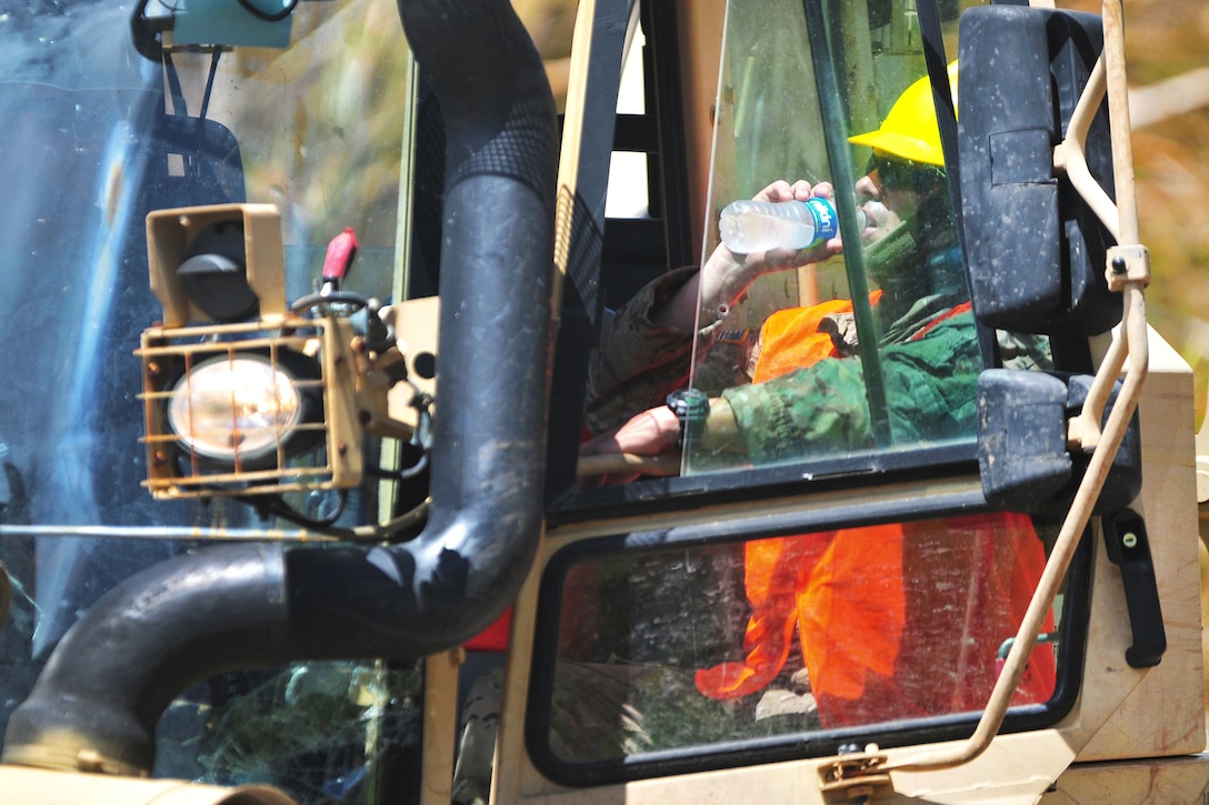 A Guardsman drinks water in a bulldozer's cab.