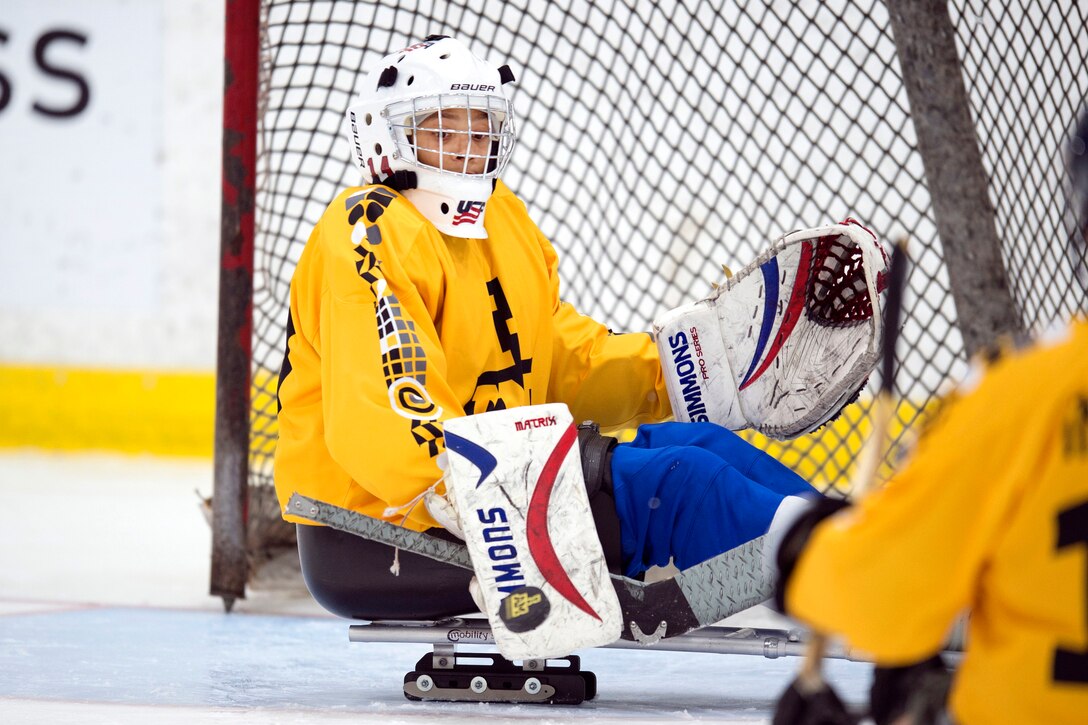 A hockey player sitting in a sled guards the goal.
