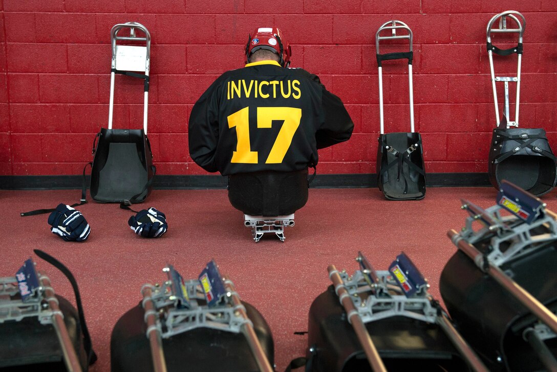 A sled hockey player sits in a sled surrounded by hockey equipment.