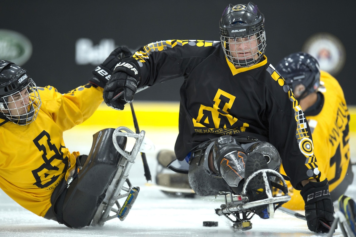 A sledge hockey player pushes another sledge hockey player.