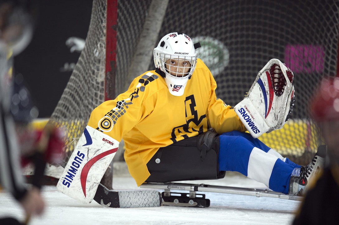 A sled hockey player catches a puck before it reaches a goal.