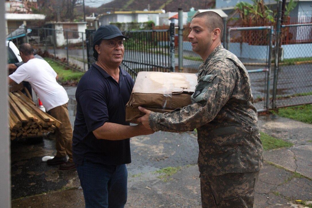 A soldier helps move boxes of tarps into a community building.