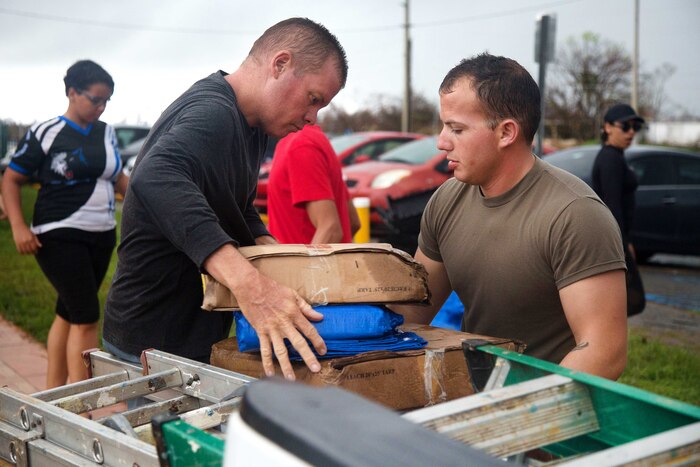 A soldier helps move boxes of tarps into a community building.