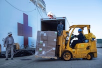 Sailors and civilians load supplies onto a hospital ship.