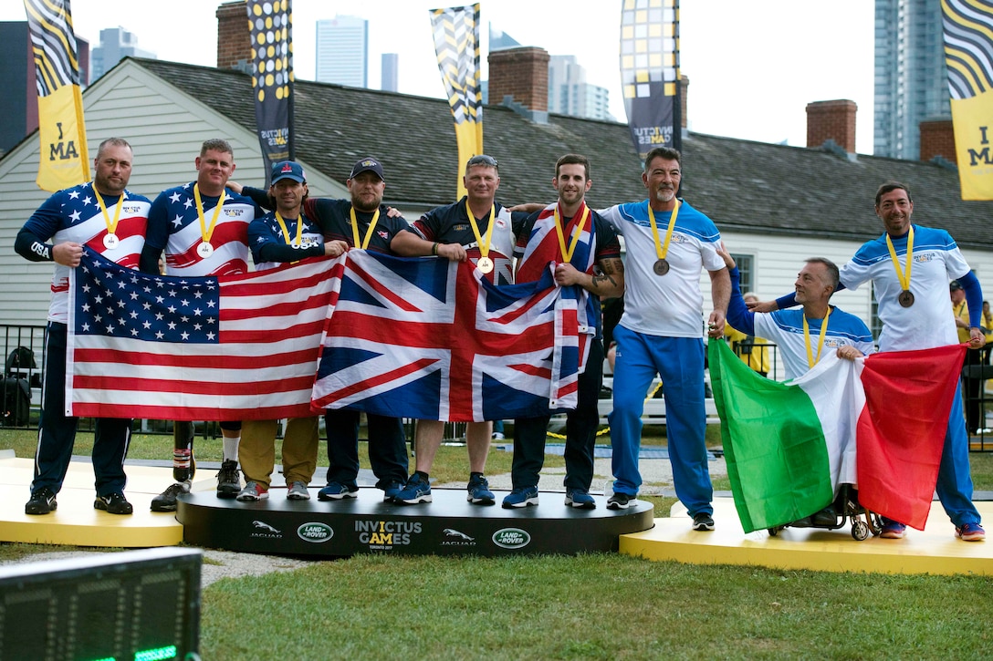 Team U.S. members pose for a photograph at the podium with members of Team Great Britain and Team Italy after being awarded the silver medal in archery.