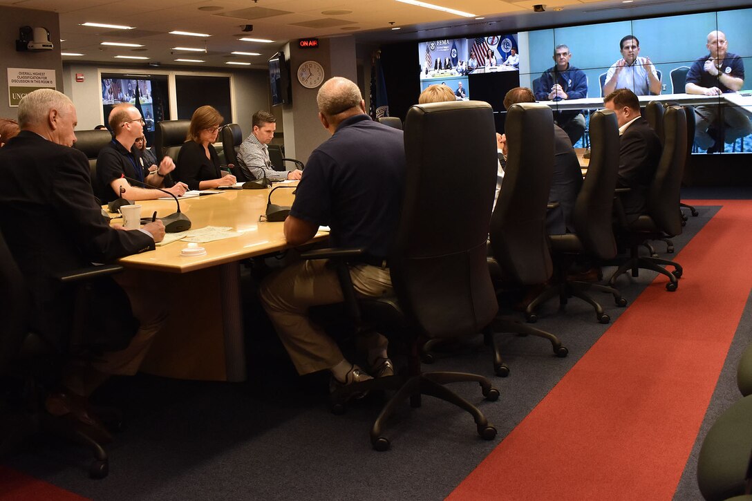 The vice president sits at the head of a table with a group of people looking at teleconference screens.