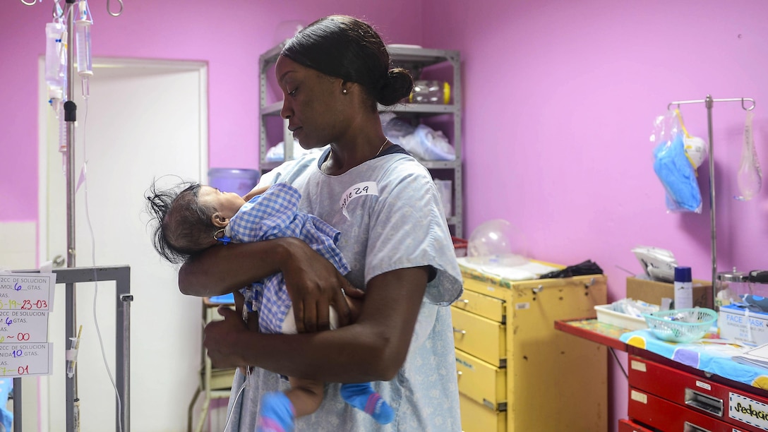 A sailor holds an infant in a hospital room.