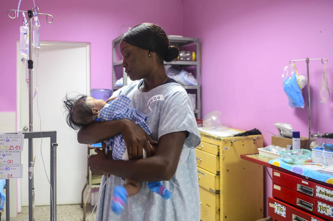 A sailor holds an infant in a hospital room.