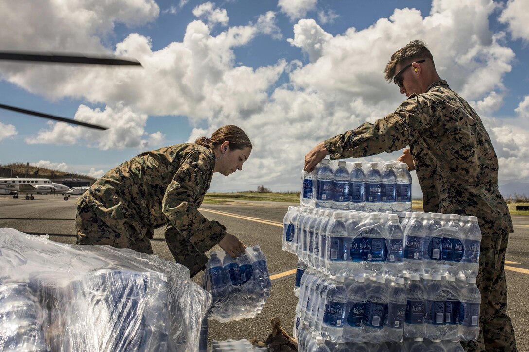 Two Marines unload and stack cases of water