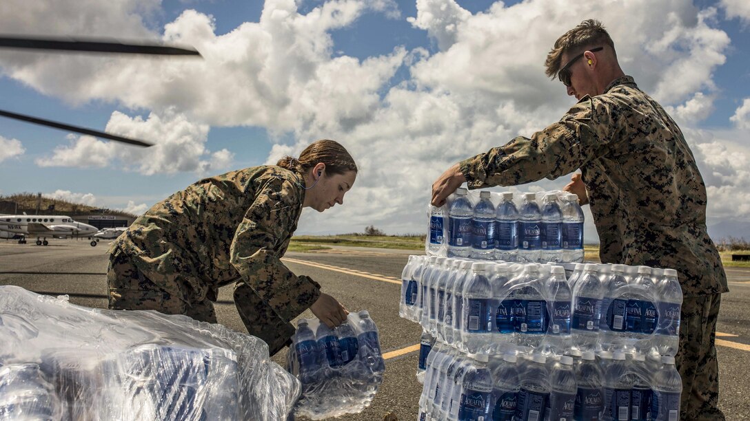 Two Marines unload and stack cases of water