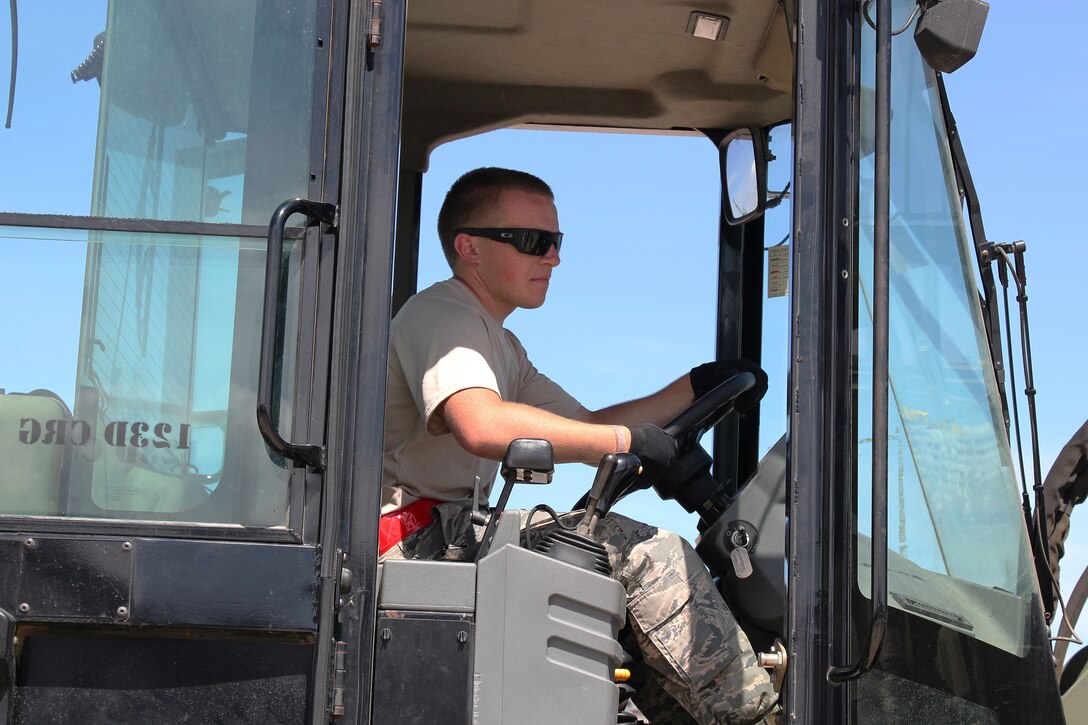 An airman sits at the controls of a forklift.