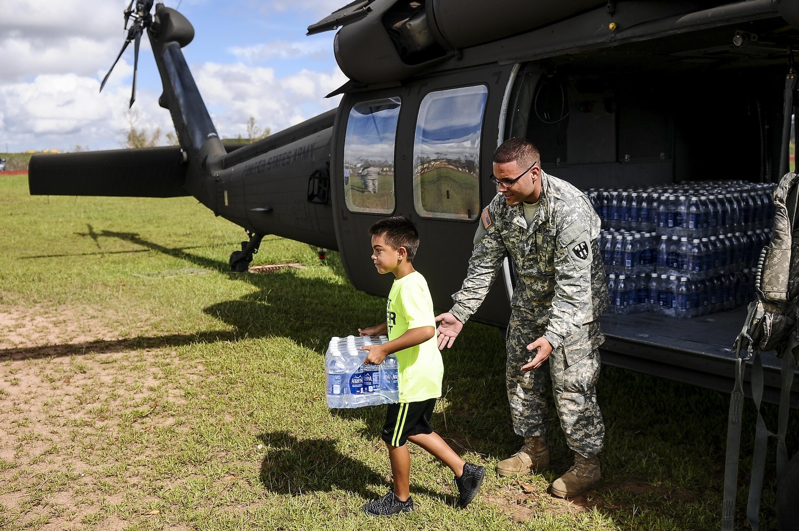 A soldier watches a child carrying a case of water away from a helicopter.