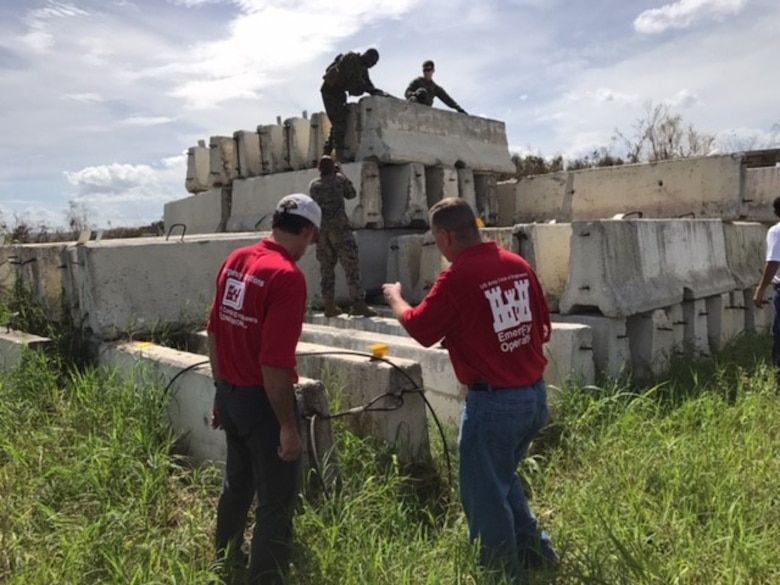 U.S. Army Corps of Engineers personnel attach cables to jersey barriers that will then be sling loaded by helicopters and placed at the bottom of the dam.