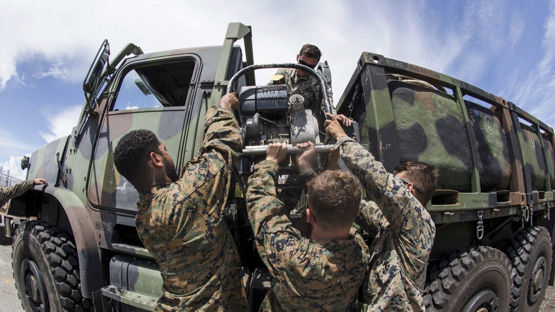 Marines lower a water pump from a vehicle.