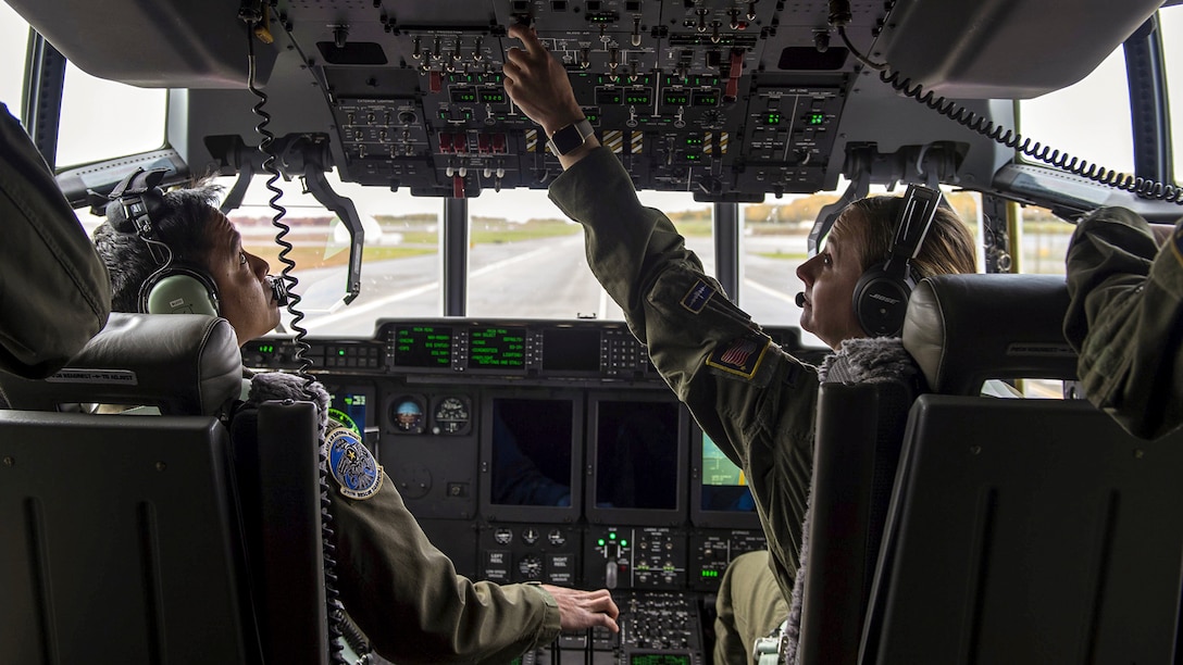 Two pilots operate controls in an aircraft cockpit.