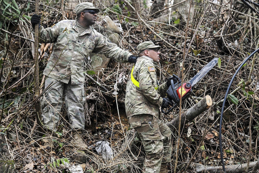 Soldiers use a chainsaw to remove debris from a road.