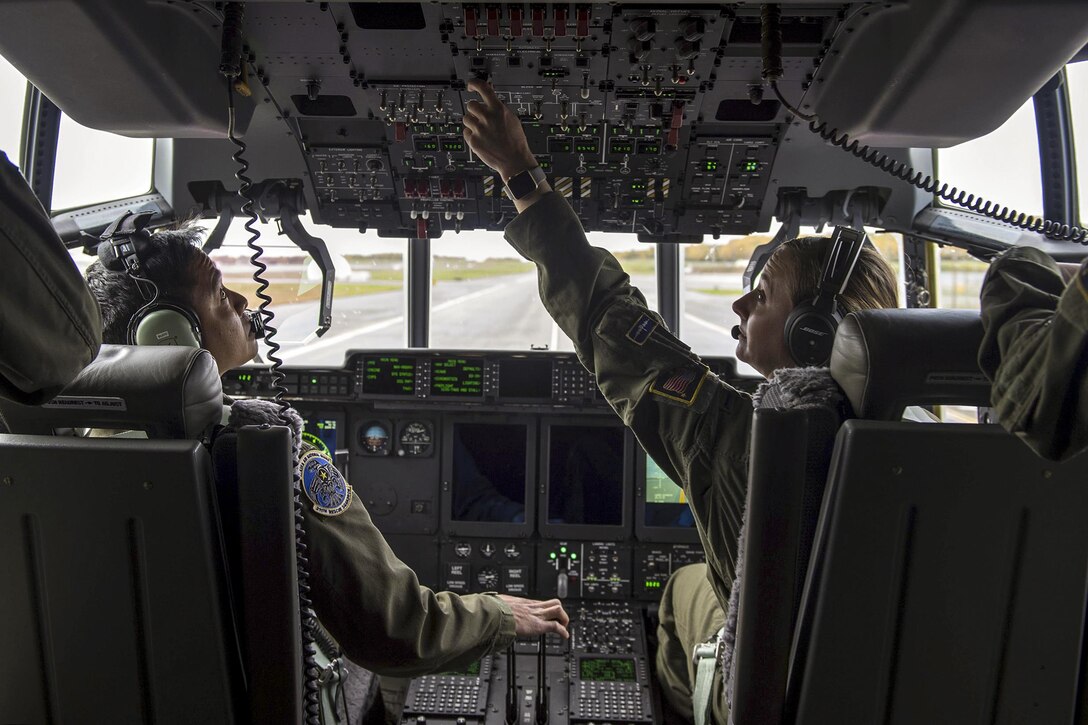 Two pilots operate controls in an aircraft cockpit.