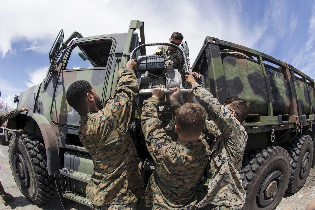 Marines lower a water pump from a vehicle.