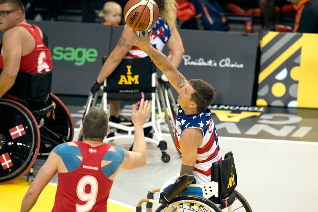 A Team U.S. member reaches for a rebound against a Danish defender in a preliminary rounds wheelchair basketball game.