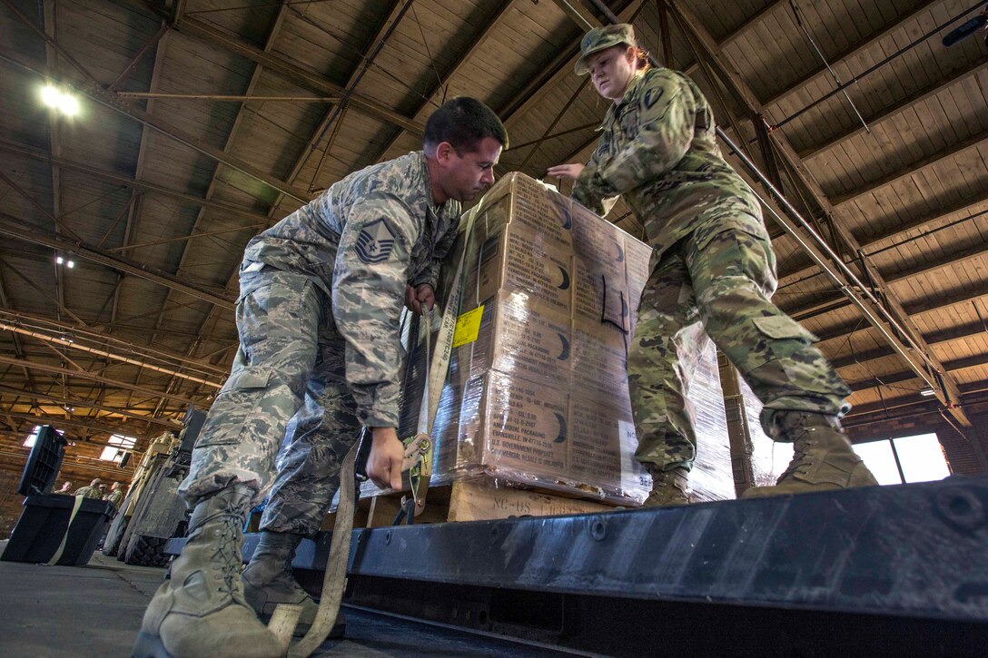 Guardsmen secure a pallet of meals ready to eat before loading it on a heavy expanded mobility tactical truck.