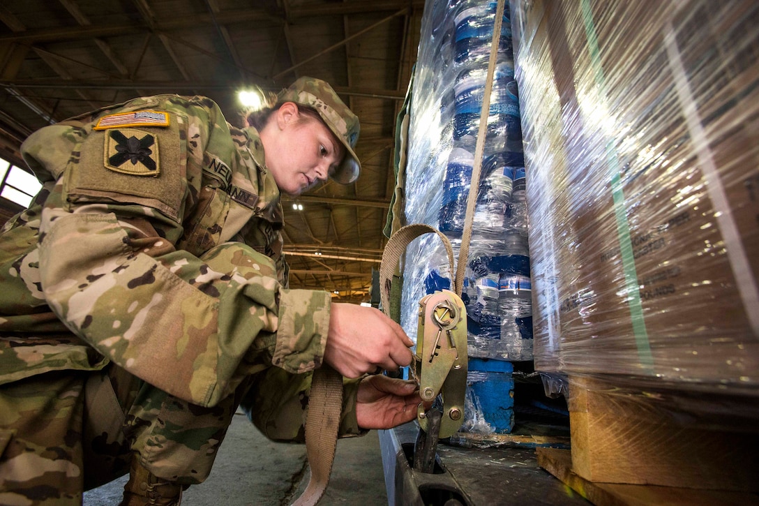 Sgt. Madeline Neumann tightens the cargo straps and clamps to a pallet of meals ready to eat before loading it on a heavy expanded mobility tactical truck.