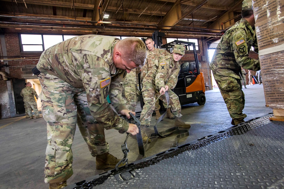 Guardsmen tighten and secure cargo straps around a large pallet of water before loading it on a heavy expanded mobility tactical truck.