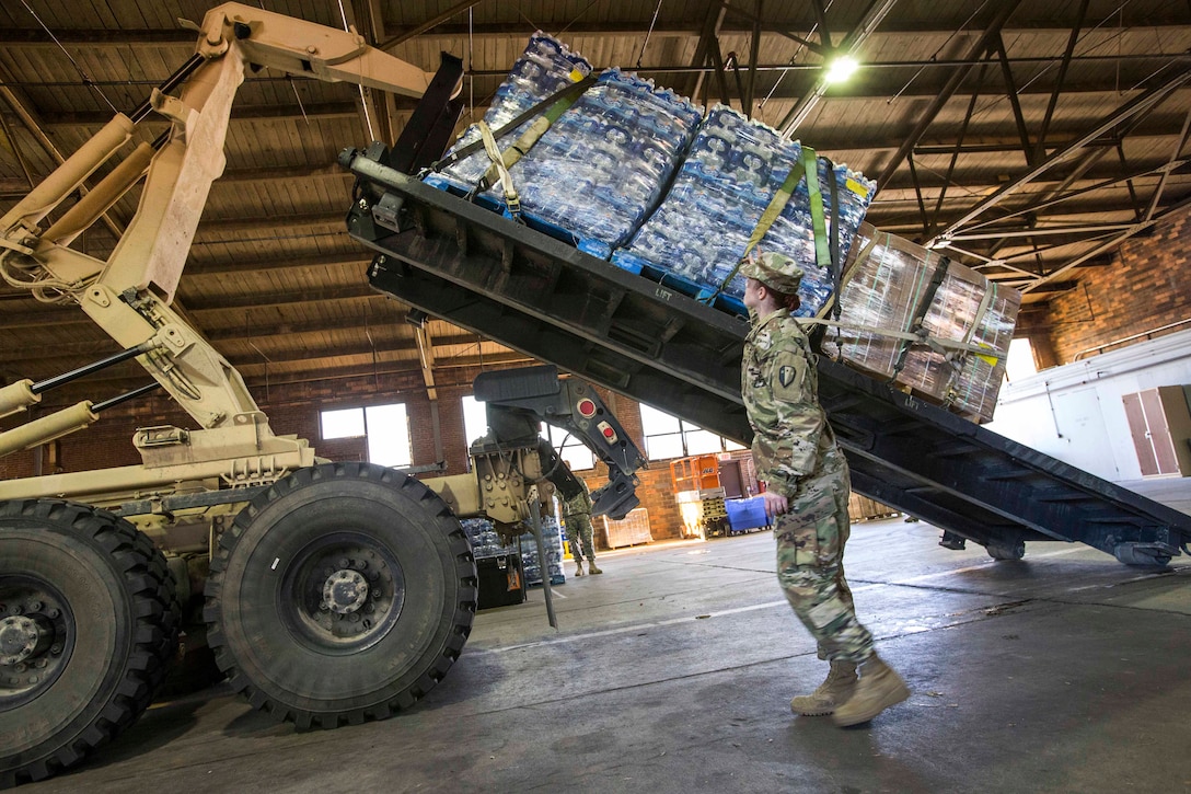 Army Sgt. Madeline Neumann directs the loading of a pallet on a heavy expanded mobility tactical truck.