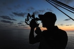 A U.S. Coast Guard Academy officer candidate practices navigating using the stars and a sextant during an evening training session aboard United States Coast Guard Barque Eagle