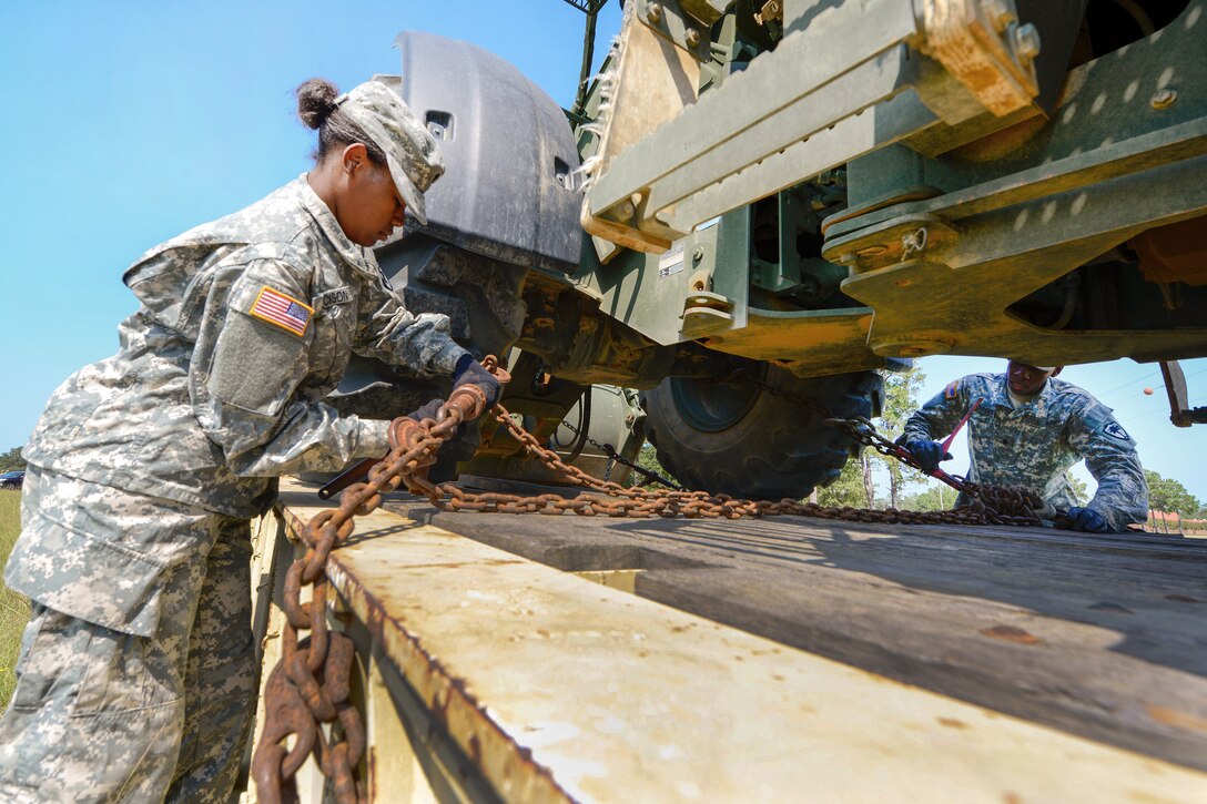 Army Spc. Lachanda Jackson unloads heavy equipment off from a flatbed truck to be transported.