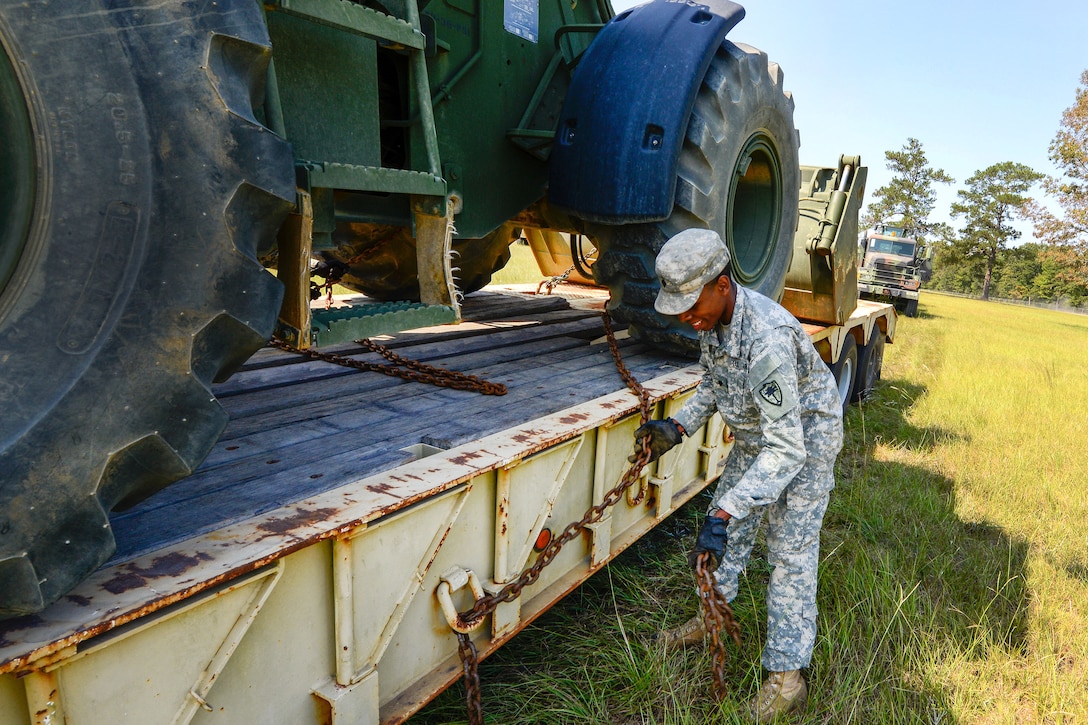 Army Spc. Marcus Robinson unloads heavy equipment off from a flatbed truck.