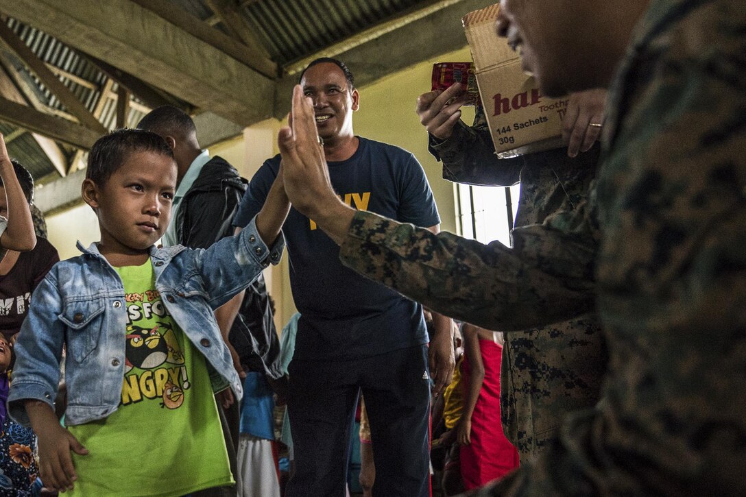 A sailor high-fives a child in a room.