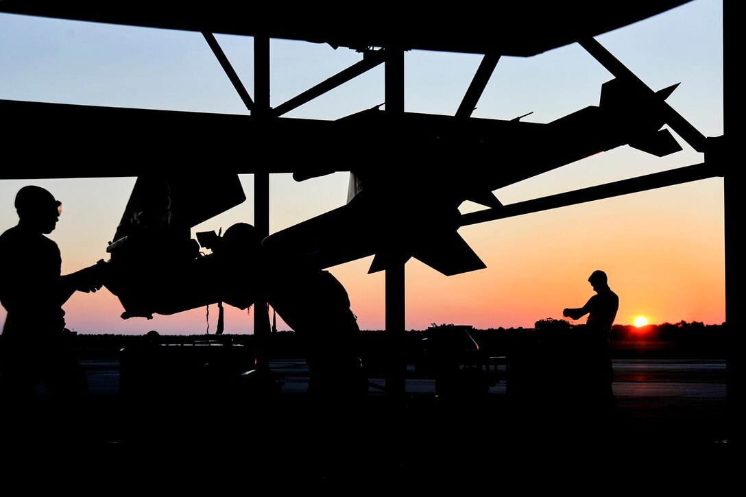 Three silhouetted airmen work on an aircraft.