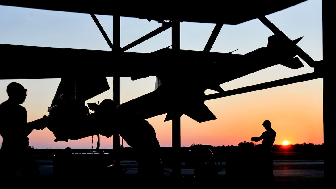 Three silhouetted airmen work on an aircraft.