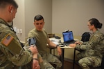 Mobile Medic Spc. Amanda Knight sets up a video chat with a medical provider while Mobile Medic Spc. Joshua Rath checks Spc. Joao Dos Santos Faustino's vitals during an early morning sick call at the 232d Medical Battalion Sept. 25. A team of mobile medics stationed at the battalion, use a combination of virtual and hands-on health care to triage the Soldiers who report to morning sick call.