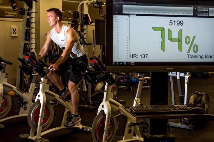 A person is on a stationary bike with a screen showing 74%.