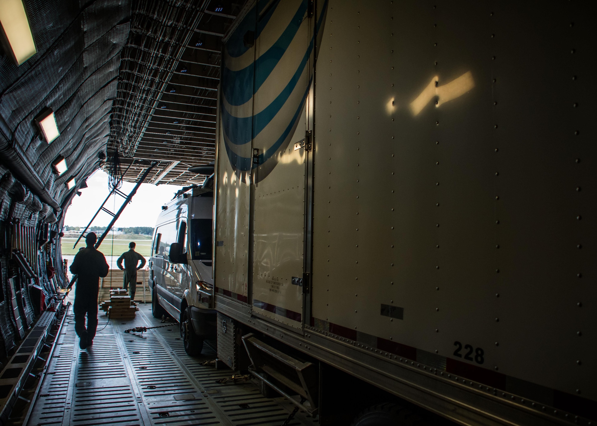 Aircrew members walk through the cargo bay of a C-5M Super Galaxy from Dover Air Force Base, Del. as aerial porters finish loading it at Dobbins Air Reserve Base, Ga. Oct. 2, 2017. Airmen loaded three AT&T trucks: one emergency communication vehicle and two satellite cell on light trucks. These trucks will be used to provide Wi-Fi, LAN lines, and Plain Old Telephone Service (POTS) lines to Puerto Rico in the wake of Hurricane Maria’s destruction. (U.S. Air Force photo/Staff Sgt. Andrew Park)