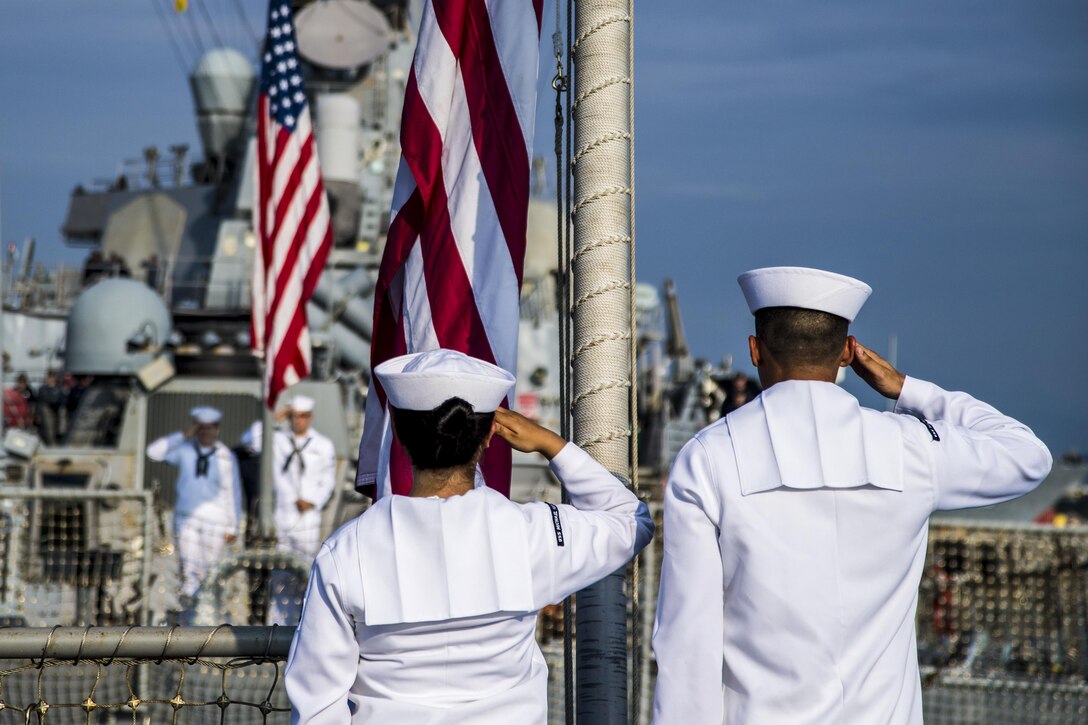 Sailors salute the flag at half mast on a ship.
