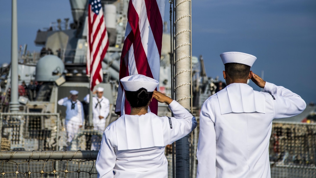 Sailors salute the flag at half mast on a ship.