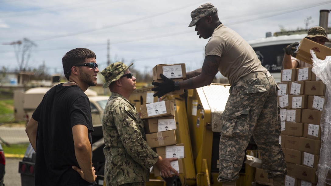 A sailor and soldier unload pallets of relief supplies.