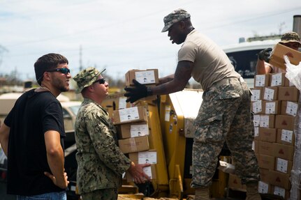 A sailor and soldier unload pallets of relief supplies.