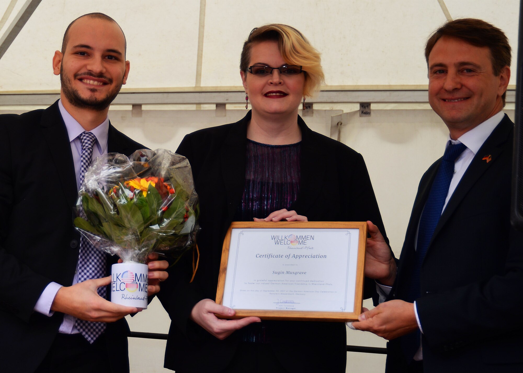 Sugin Musgrave, Kaisersluatern Military Community spouse, receives a certificate of appreciation from John Constance, left, Atlantic Academy project manager, and David Sirakov, right, director of Atlantische Akademie, in Ramstein-Miesenbach Germany, Sept. 30, 2017. Musgrave contributed her time and knowledge to support U.S. families who were adjusting to living in Germany.