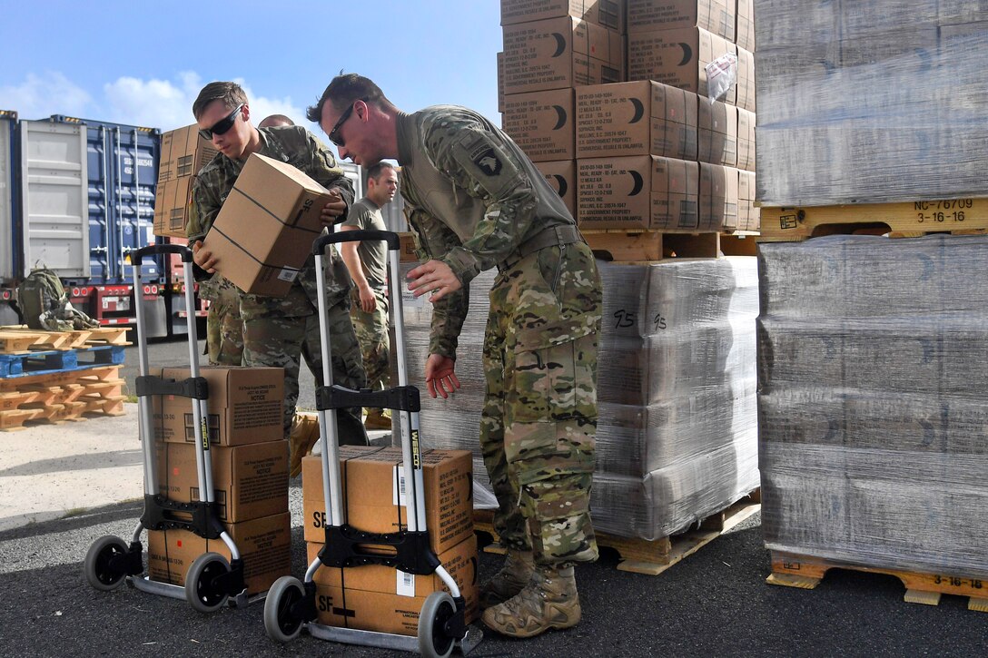Two soldiers move boxes onto handcarts.