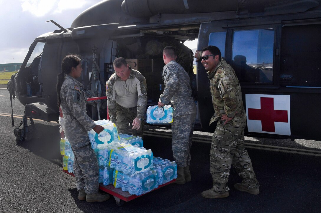 Four soldiers pick up cases of water and put them into helicopters.